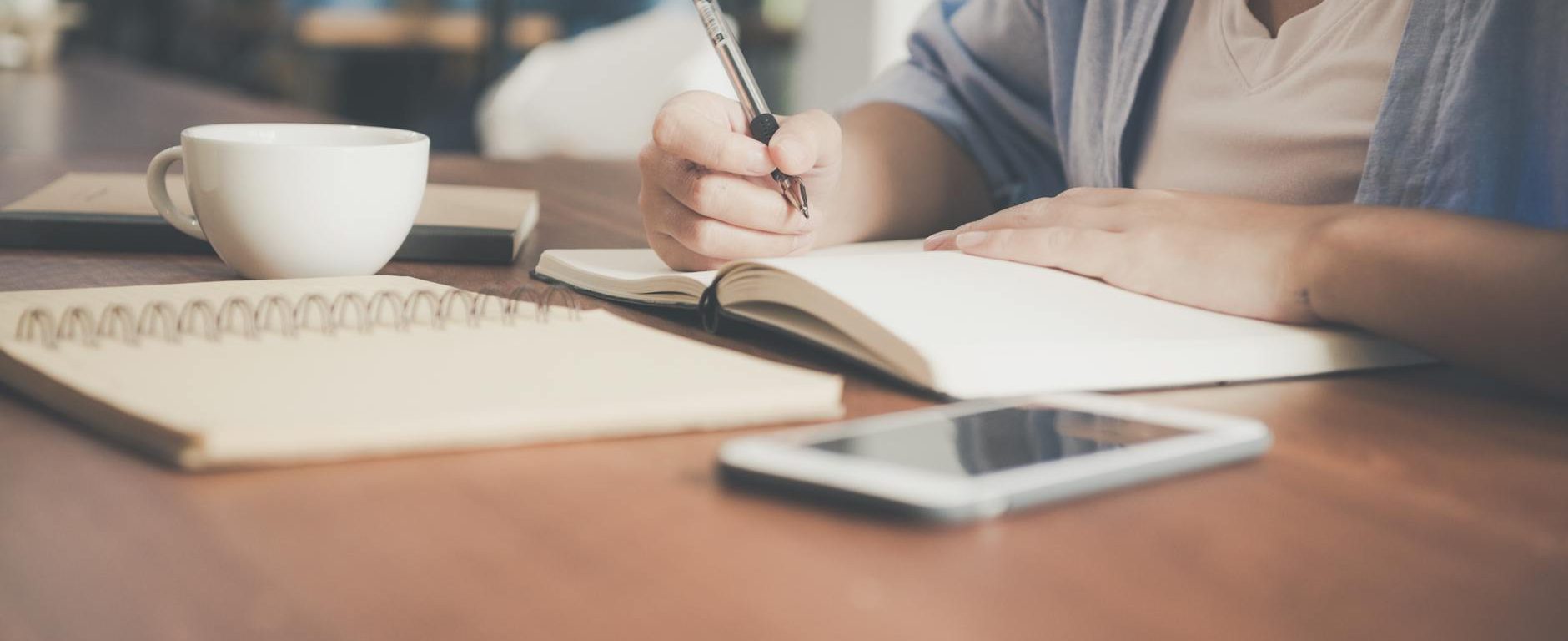 woman writing on a notebook beside teacup and tablet computer