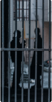 Two inmates behind bars, appearing in discussion.