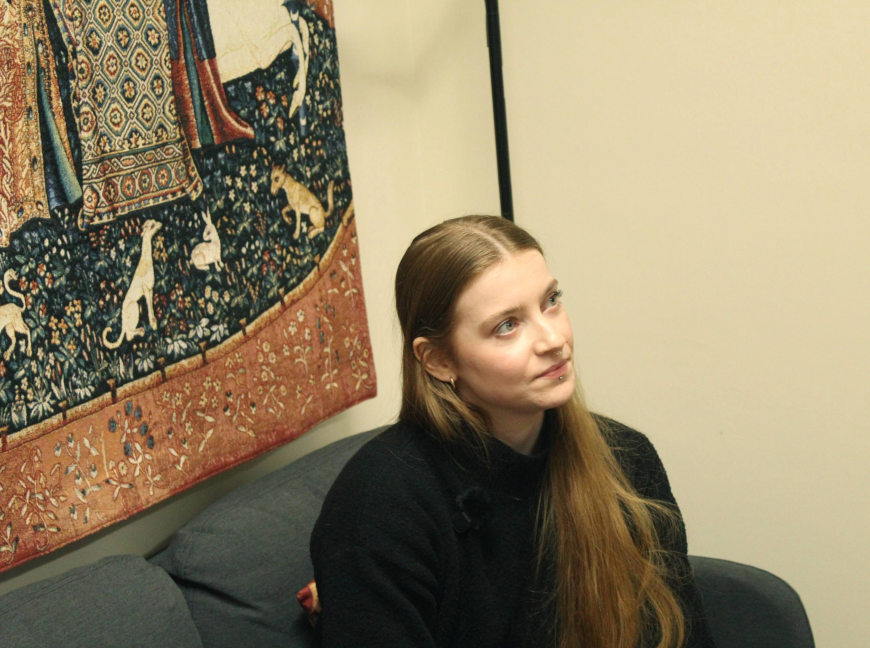 Dr. Daisy Dixon sat in front of a tapestry