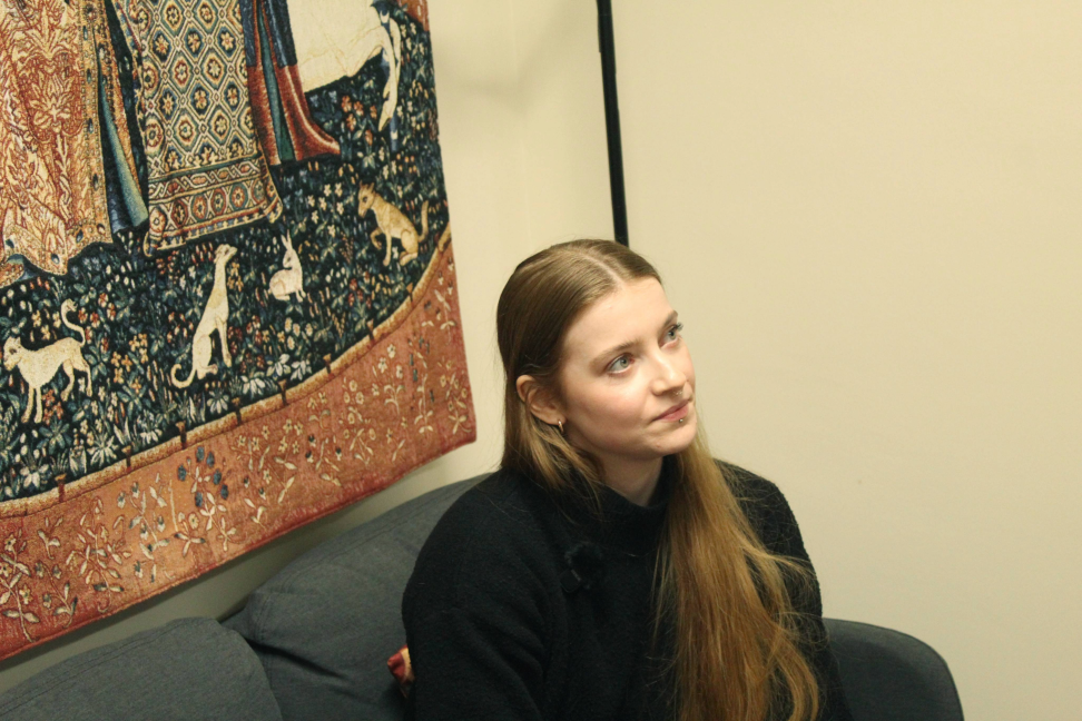 Dr. Daisy Dixon sat in front of a tapestry