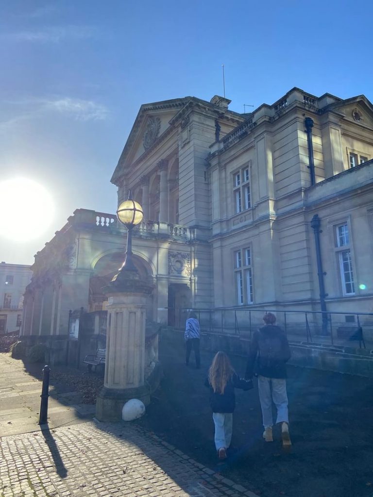 People walking down a sidewalk in front of a large regency building. 