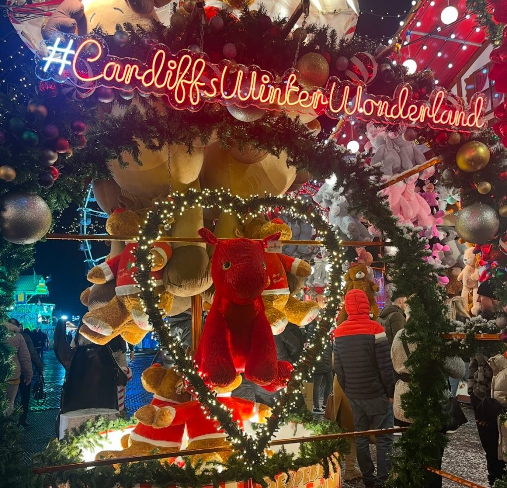 Winter Wonderland Sign with stalls and lights in the background with a Welsh Dragon teddy in the centre