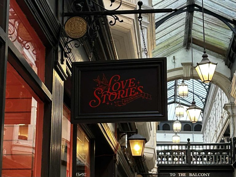 A shop sign hanging from a shop entrance with Love Stories written on it