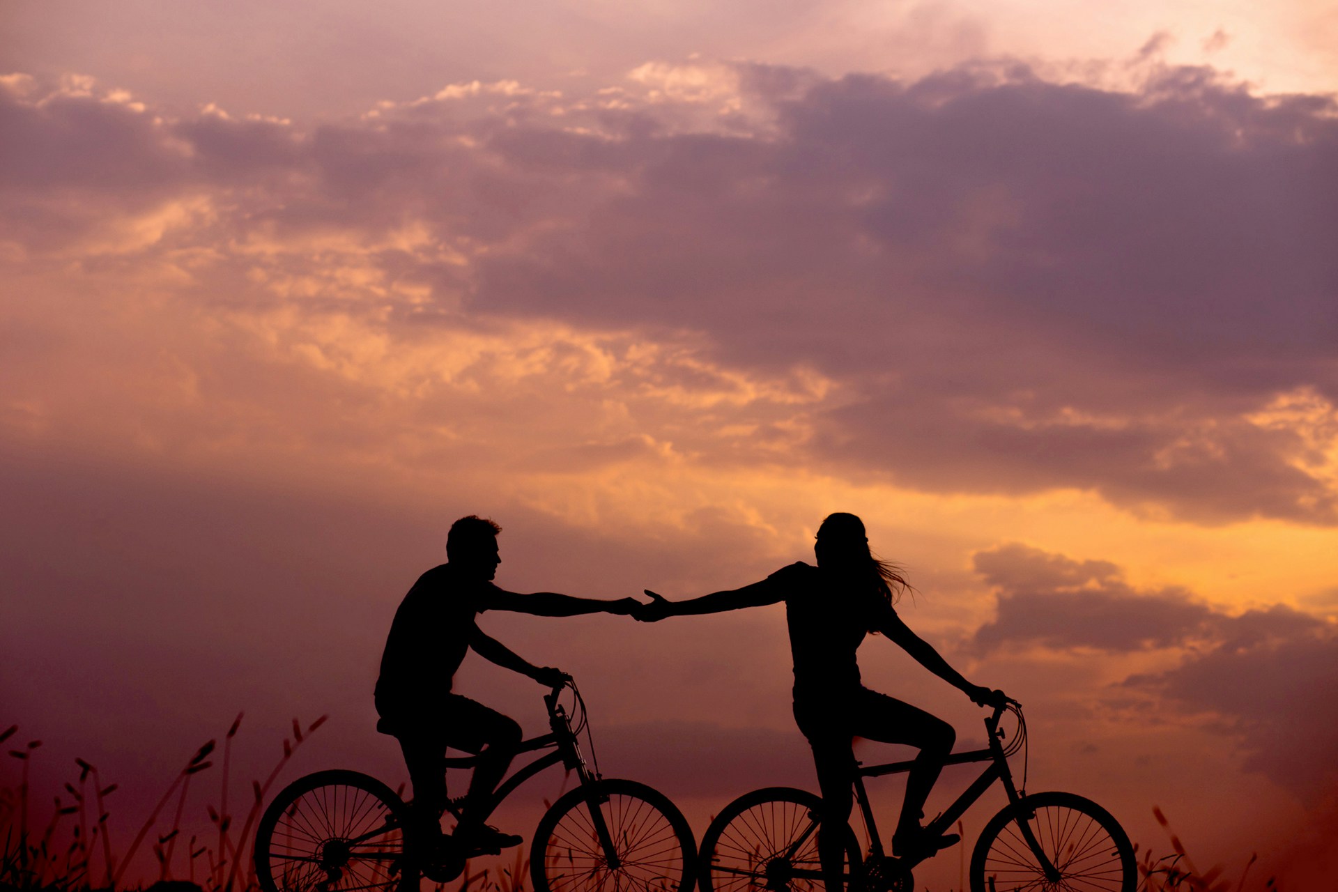two people holding hands on bikes at sunset